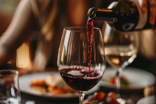 Waitress pouring red wine into glass in restaurant, closeup